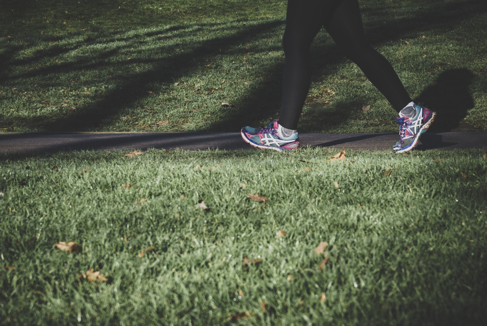 waist-down photo of person walking on sidewalk with grass around