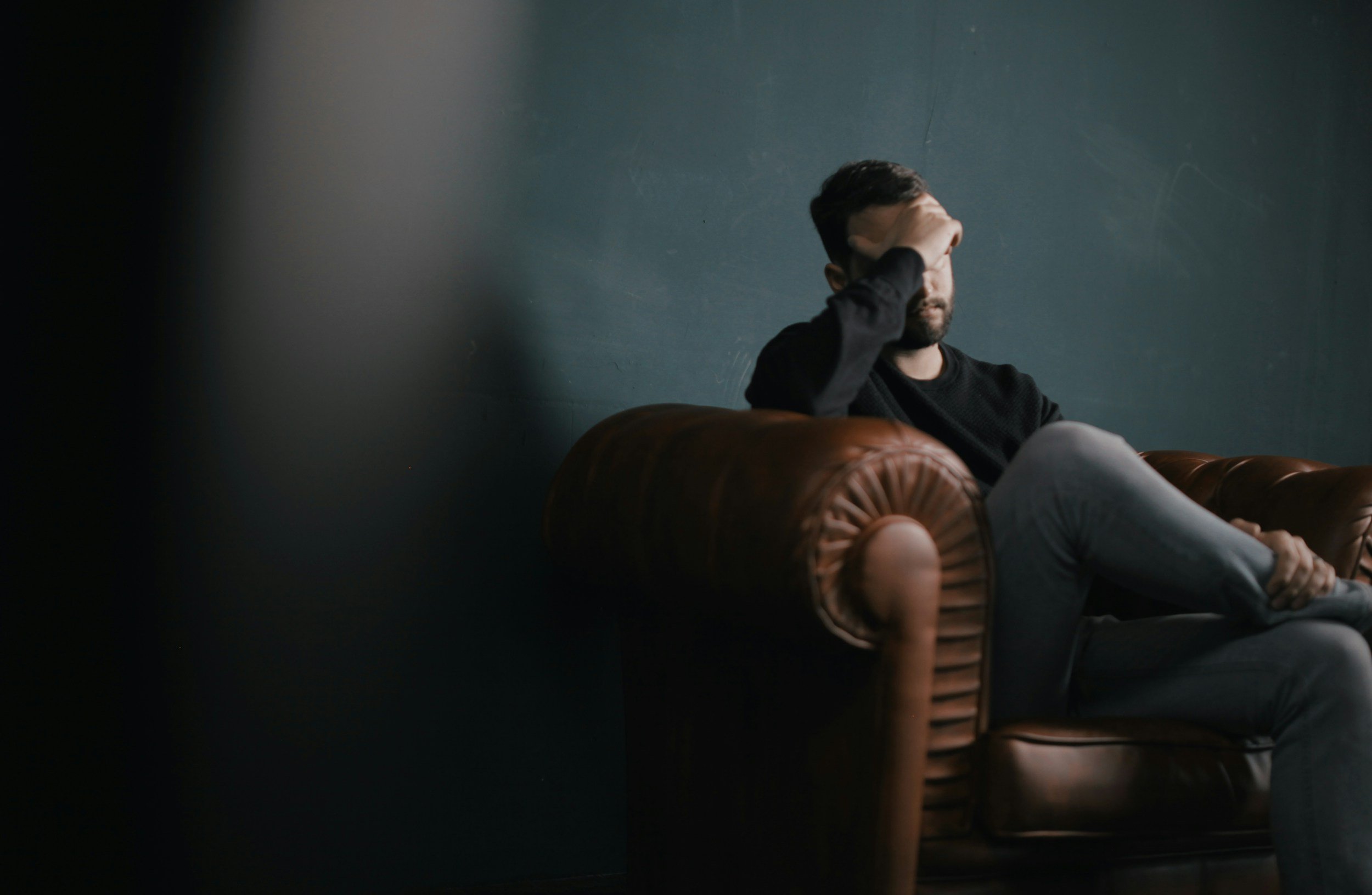 man sitting on couch with hand on head - GTWC - how masculinity and anger connect