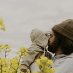 father kissing baby on cheek behind flowers- gtwc parenting blog