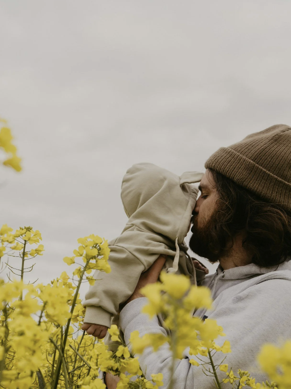 father kissing baby on cheek behind flowers- gtwc parenting blog