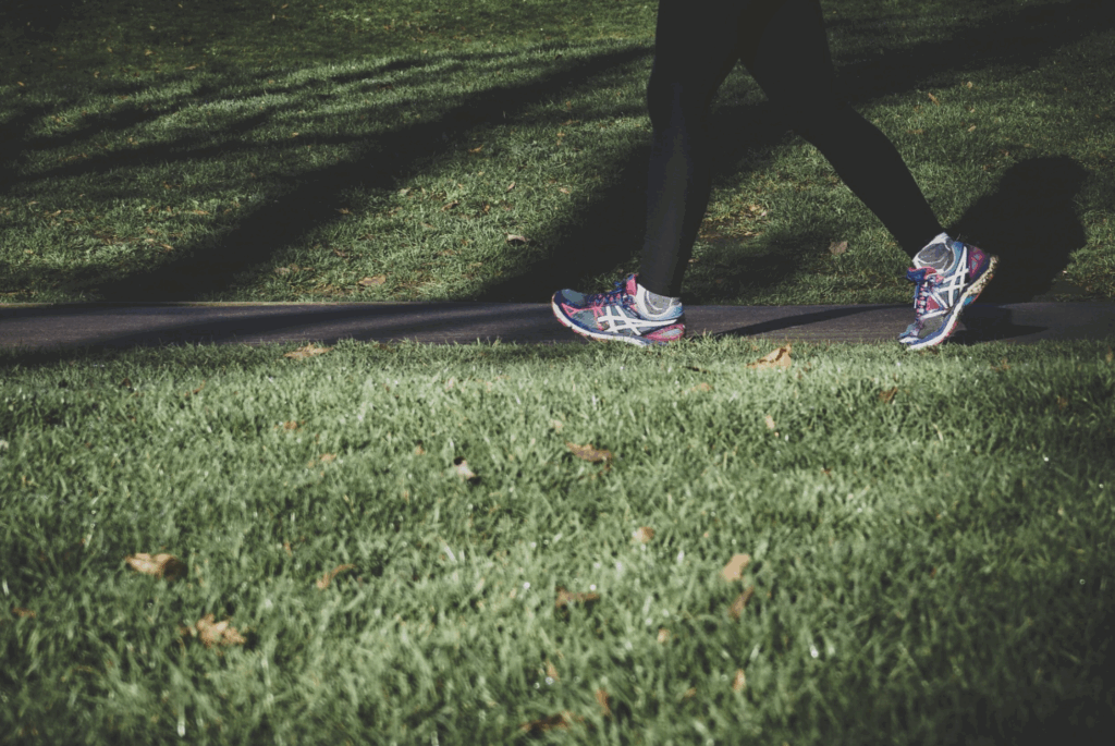waist-down photo of person walking on sidewalk with grass around